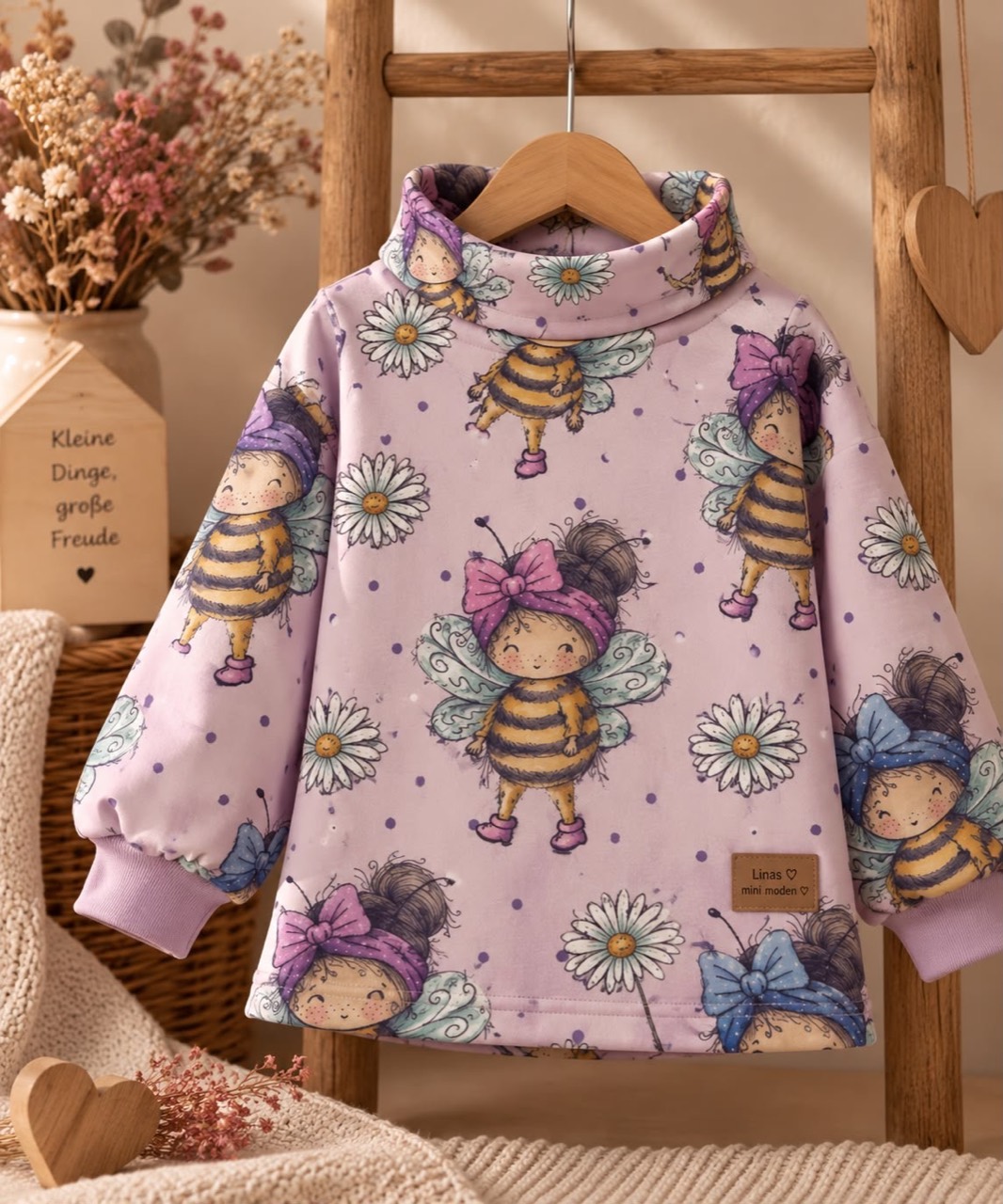 Rosafarbener Kinderpullover mit Bienenfiguren, Gänseblümchen, hohem Kragen und rosa Ärmelbündchen.